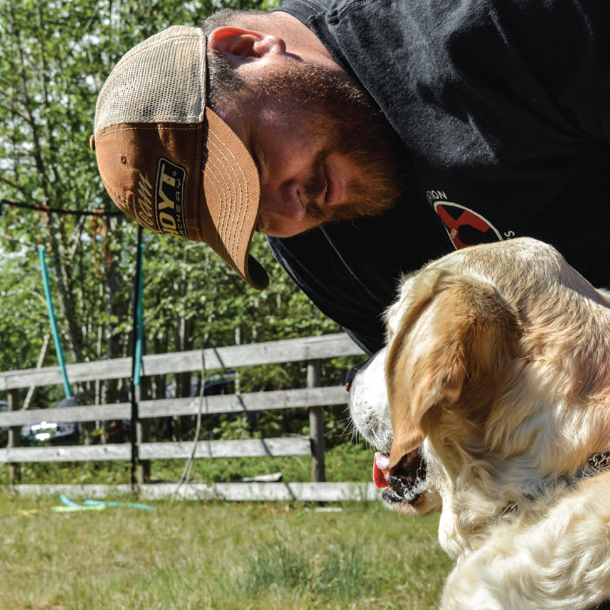 Person in a ball cap petting a golden dog
